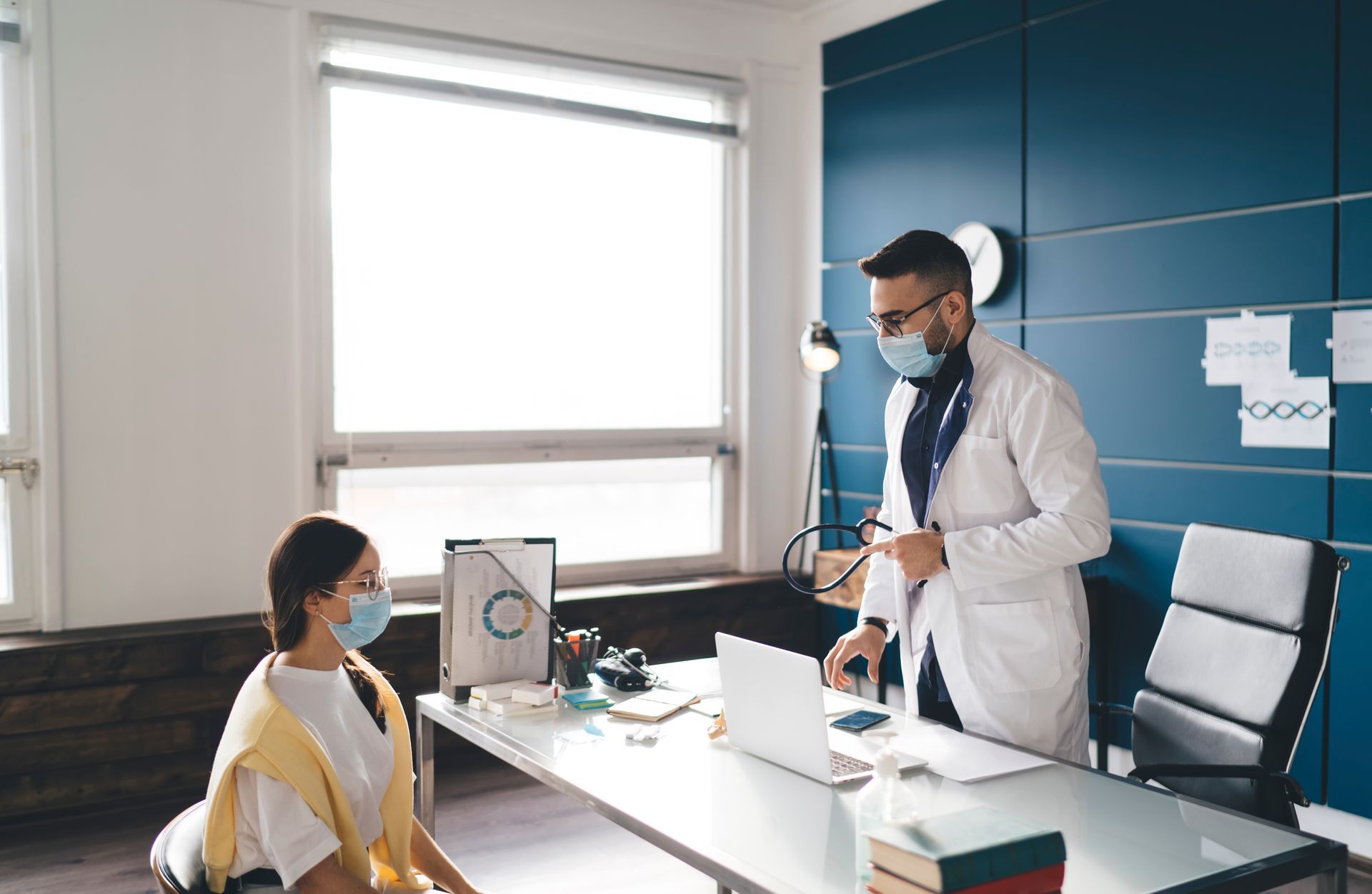 A doctor wearing a mask is talking to a patient in an office.